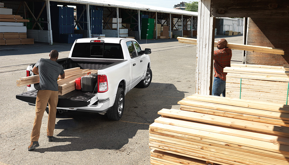 A man loading lumber into the rear tray of a RAM truck